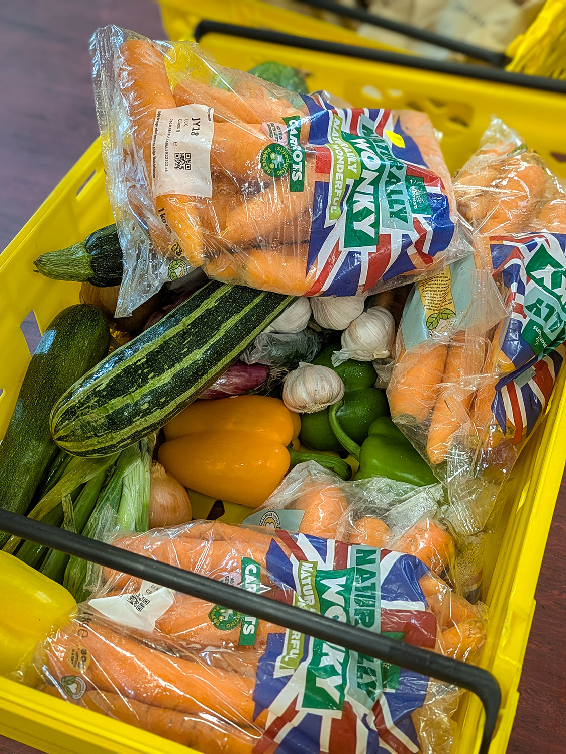 A yellow crate filled with carrots, courgettes, peppers and onions