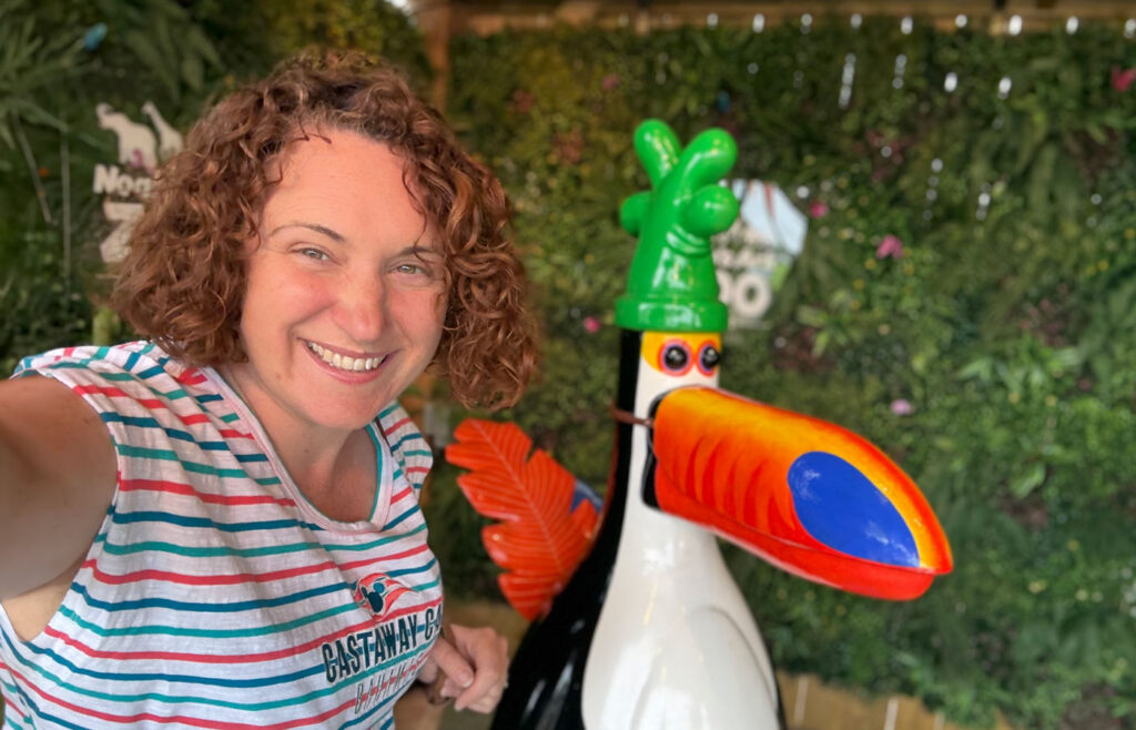 A woman with curly reddish-brown hair wears a striped sleeveless top with red, white, and teal stripes and text.