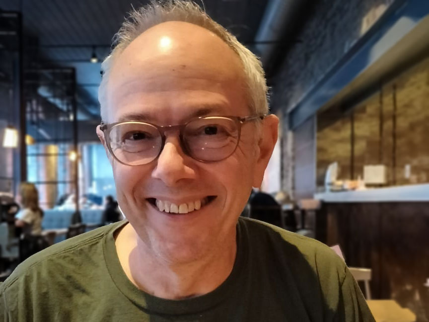 Chris Richardson, wearing a green t-shirt and glasses, is pictured smiling in a restaurant.