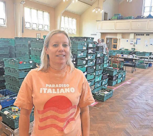 ellen foodbank appeal Ellen, wearing an orange t-shirt with "PARADISO ITALIANO" and a red sun graphic stands among stacked green plastic crates in our food bank warehouse.